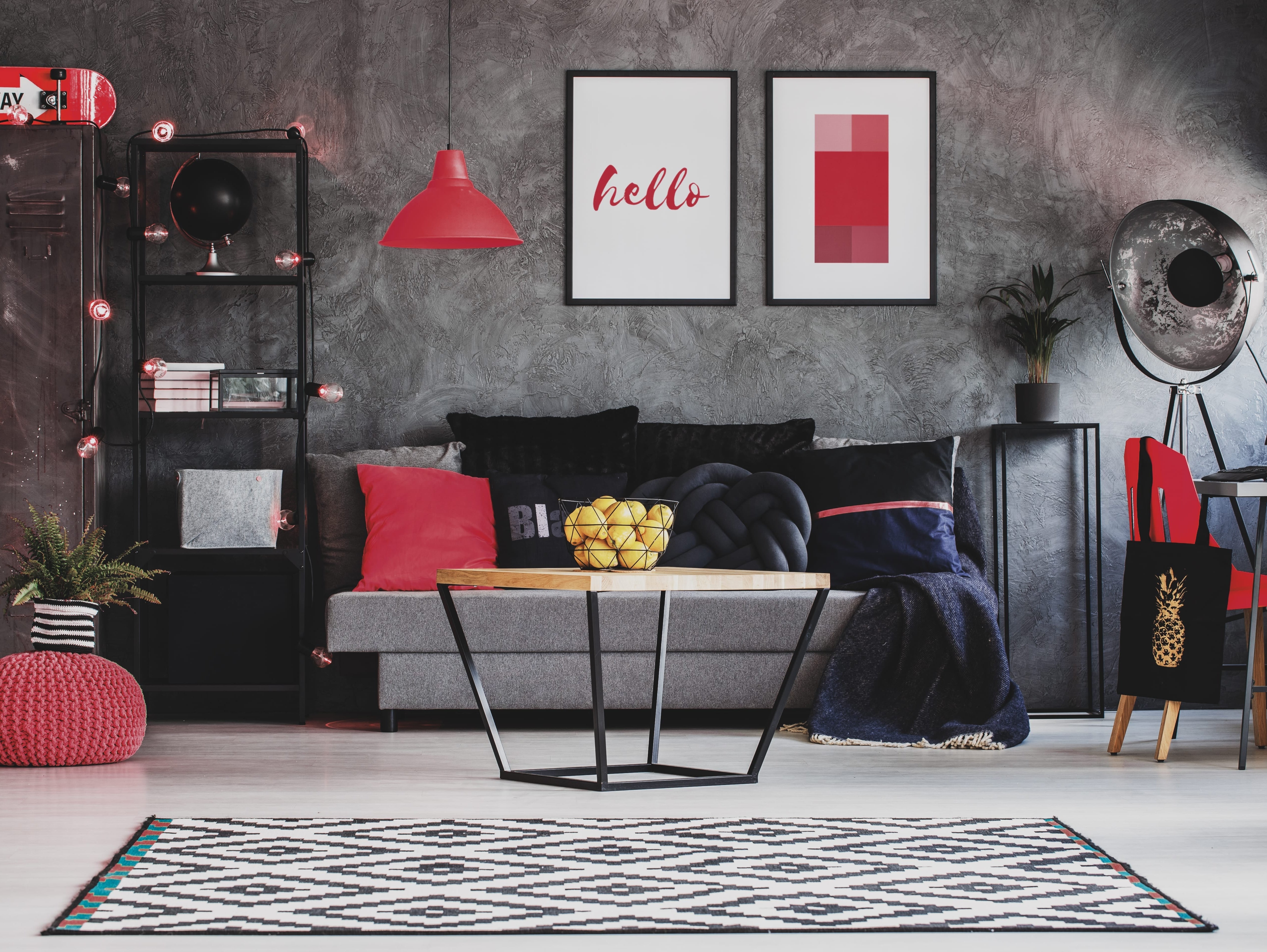 Industrial living room decor with a grey sofa, bold red accents, and a modern coffee table against a textured wall