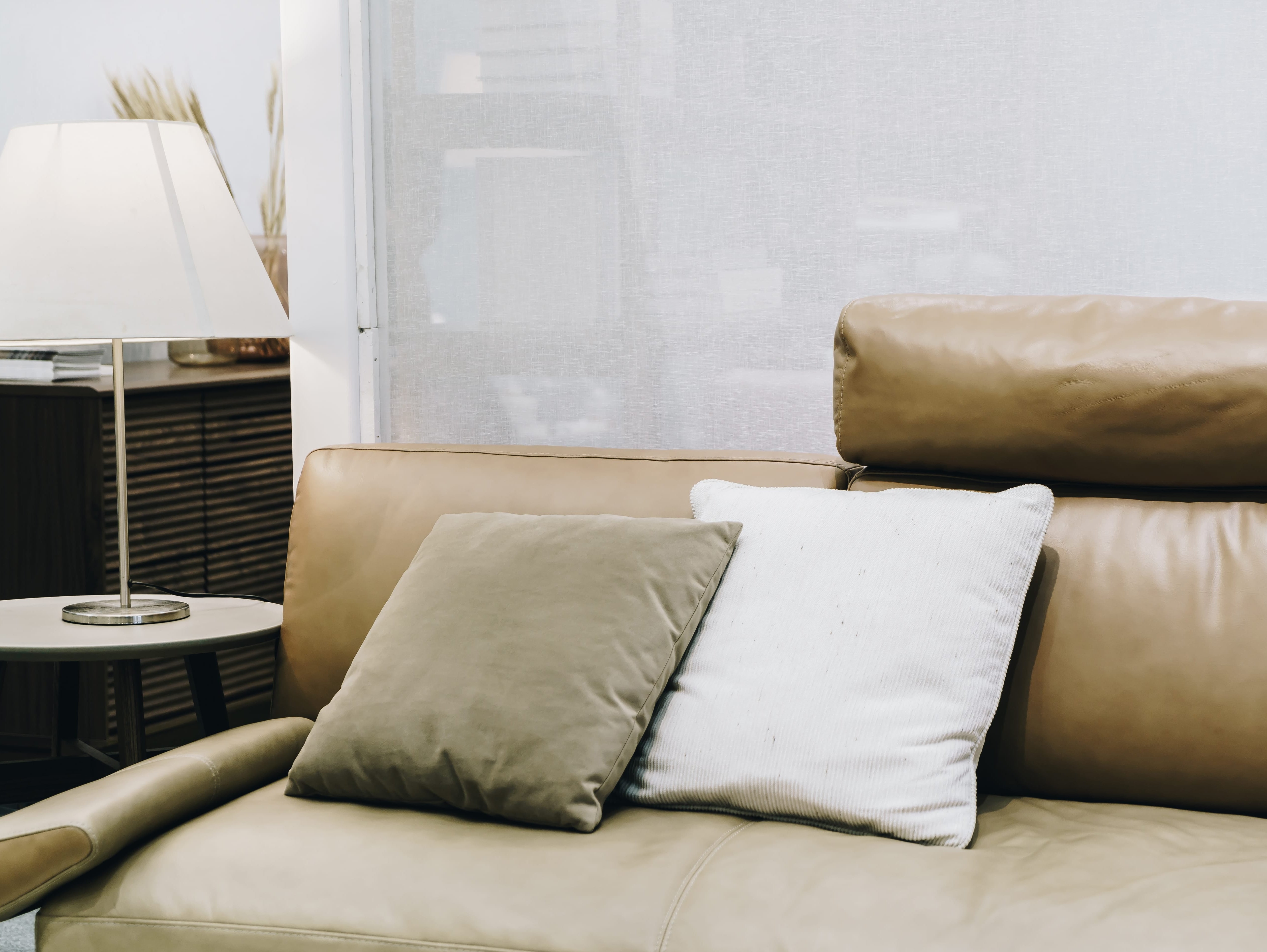 Modern tan leather sofa with accent pillows next to a lit table lamp.