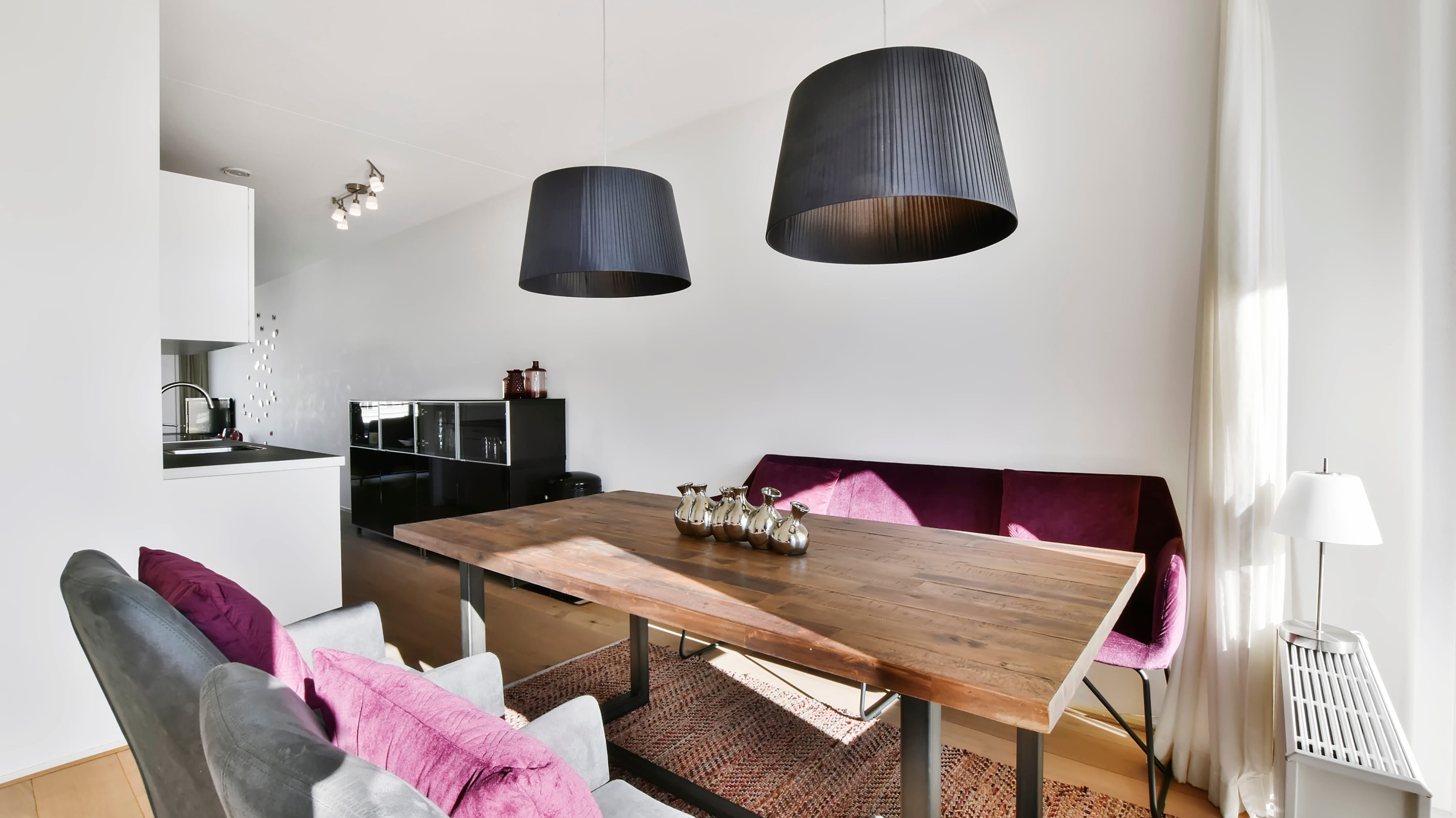 Modern wooden dining table with a purple banquette and grey chairs in a bright, open-concept home.