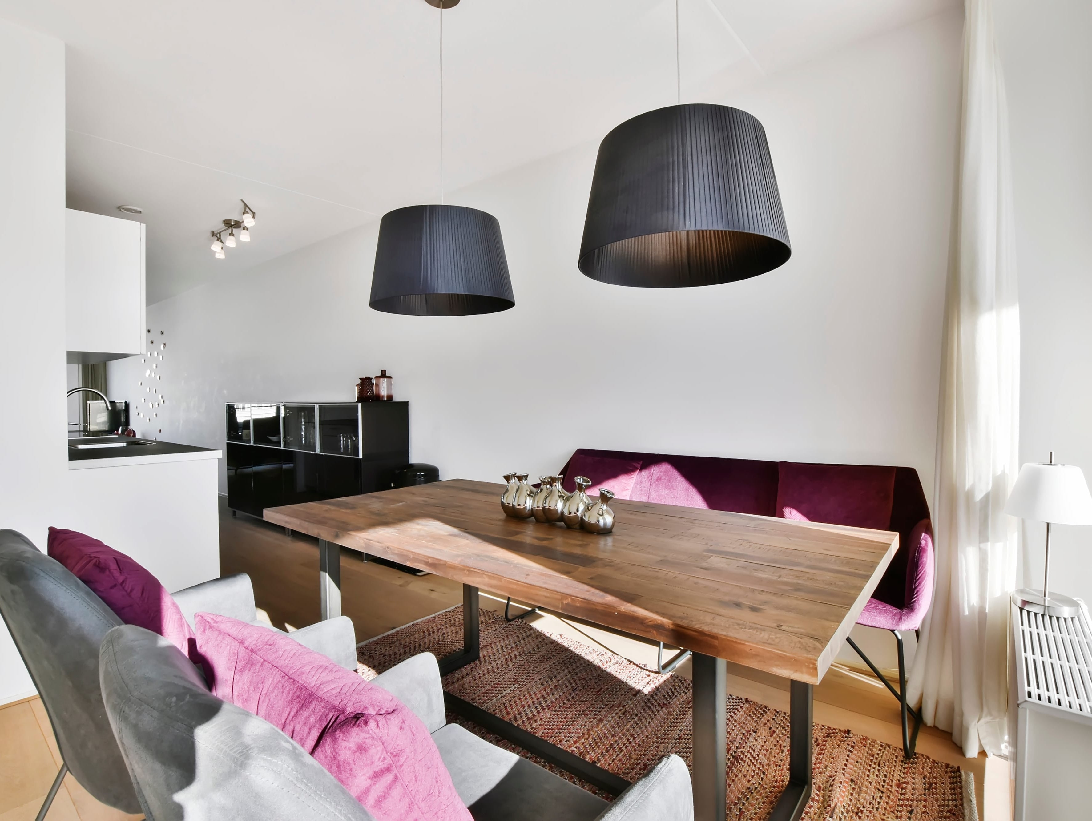 Modern wooden dining table with a purple banquette and grey chairs in a bright, open-concept home.
