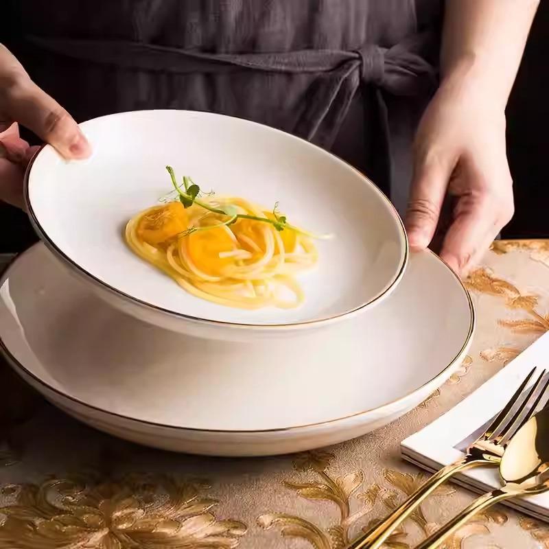 Gold-rimmed flat plate in white, lifestyle shot showing the plate with pasta on a styled table