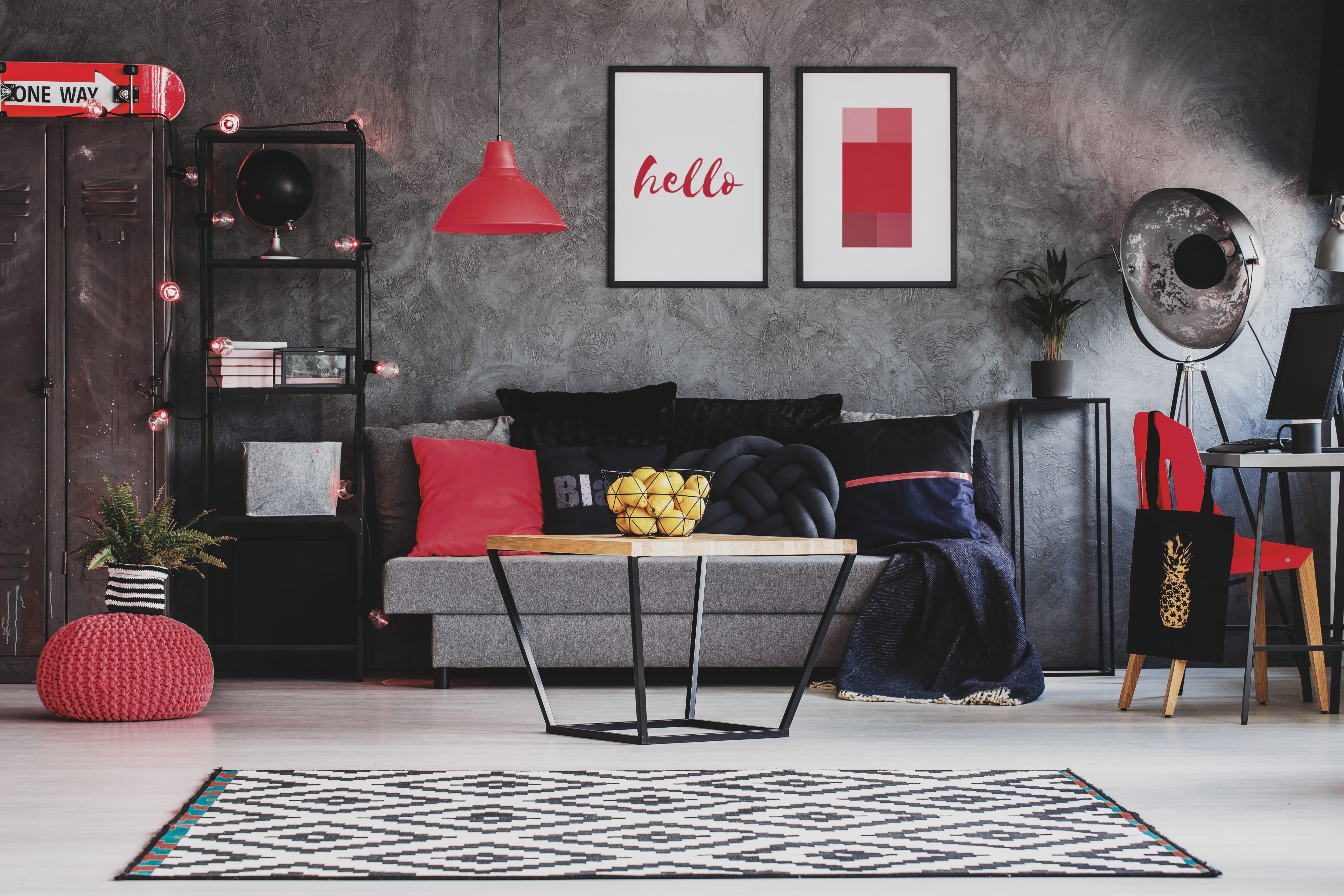 Industrial living room decor with a grey sofa, bold red accents, and a modern coffee table against a textured wall
