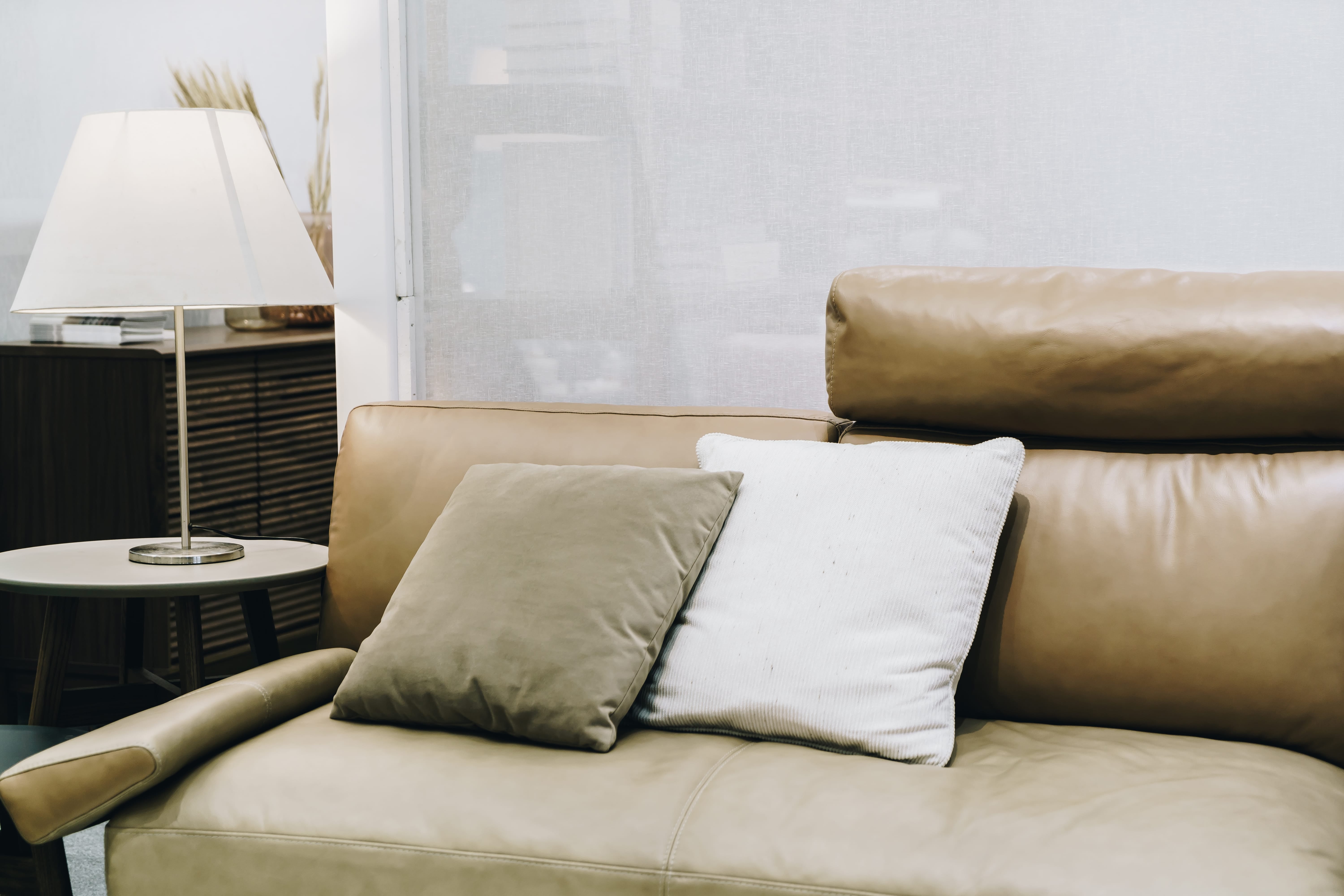 Modern tan leather sofa with accent pillows next to a lit table lamp.