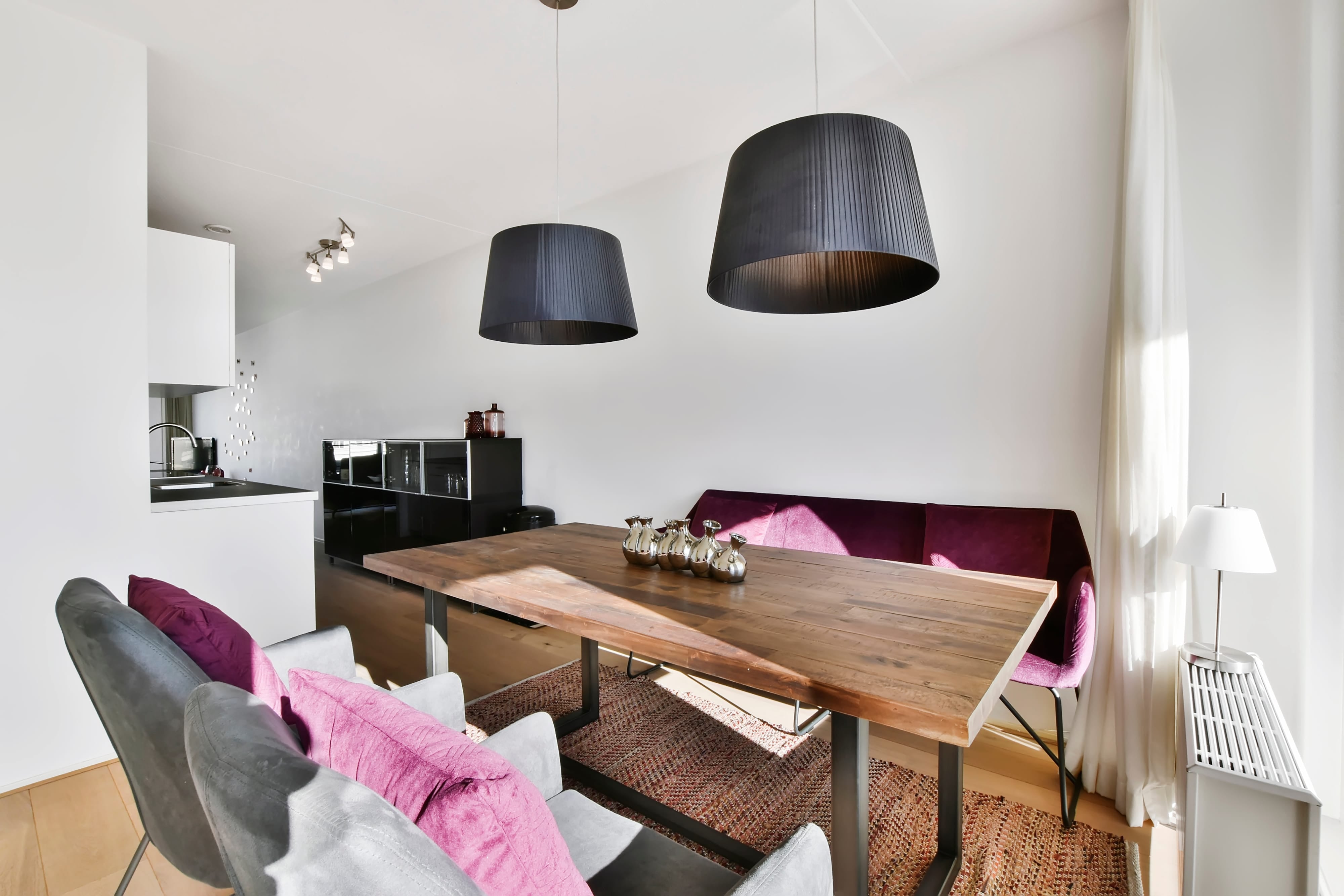 Modern wooden dining table with a purple banquette and grey chairs in a bright, open-concept home.