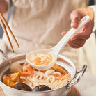Convenient soup spoon in white, lifestyle shot showing the spoon scooping noodle soup from a pot