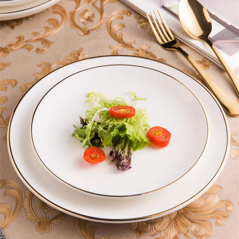 Gold-rimmed flat plate in white, lifestyle shot showing the plate with a salad and cutlery on a styled table